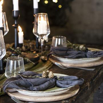 Stofserviet foldet på tallerken med kogler. Stofservietten er grå og er lavet i bomulds materiale.