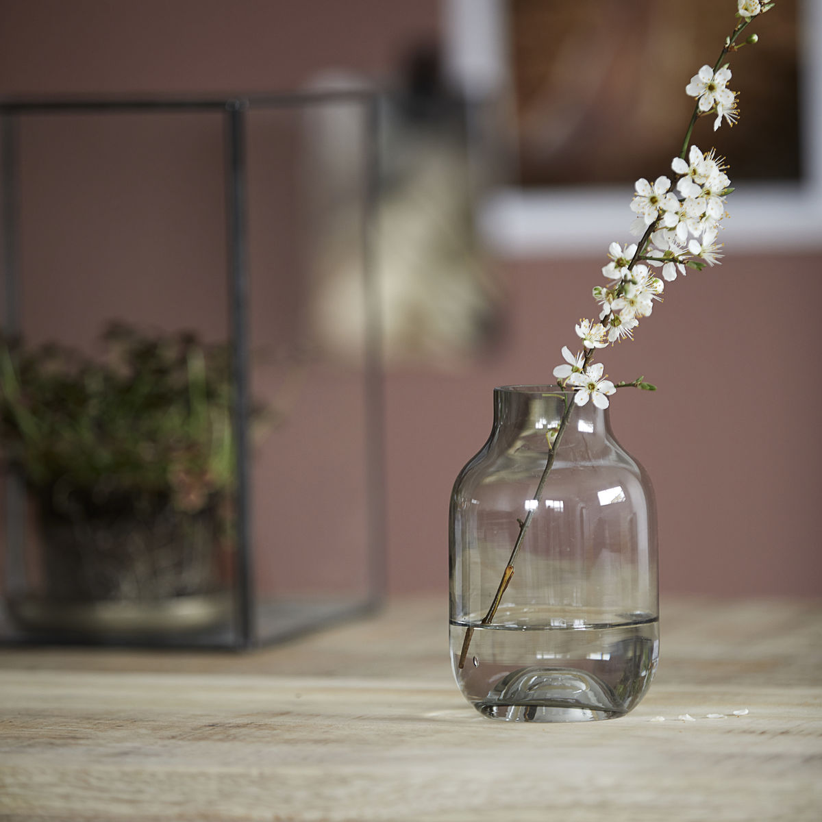 Vase i smoke farve. Den grålige nuance giver en flot kontrast til de ellers ofte klare vaser og spiller med de omkringliggende farver så som kontrasten ved de hvide blomster.