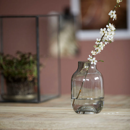 Vase i smoke farve. Den grålige nuance giver en flot kontrast til de ellers ofte klare vaser og spiller med de omkringliggende farver så som kontrasten ved de hvide blomster.