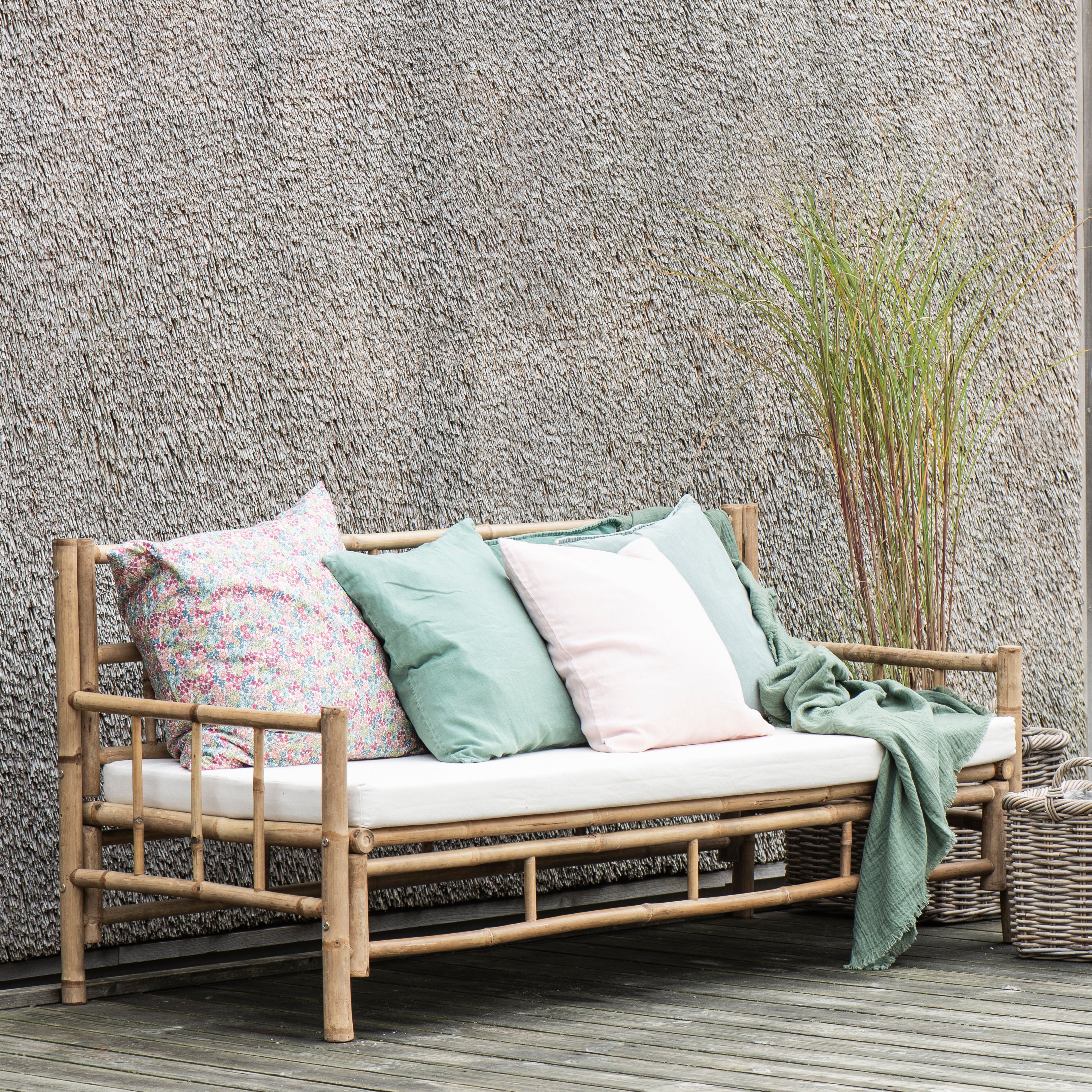 Bambus sofa med puder og tæppe på terassen.  Bambus sofaen kan bruges som loungesæt inde og ude.