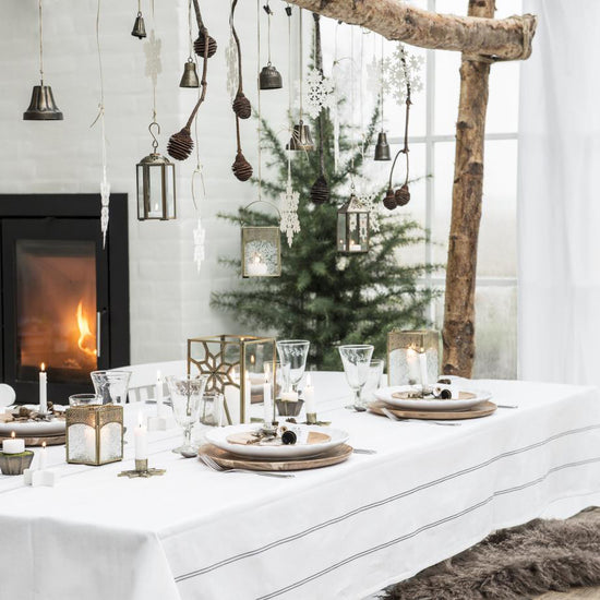 Juleklokker hængt op som dekoration over bordet med kogler og lys.